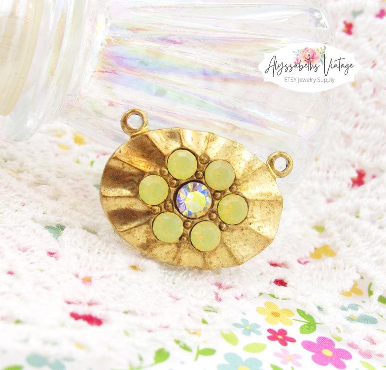 May include: Gold-toned oval pendant with a raised, scalloped edge. The pendant features a cluster of seven pale green rhinestones, with a smaller clear rhinestone in the center.