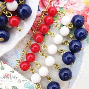 May include: A strand of red, white, and blue beads with gold chain links. The beads are strung in a cascading pattern, with the red beads at the top, the white beads in the middle, and the blue beads at the bottom.