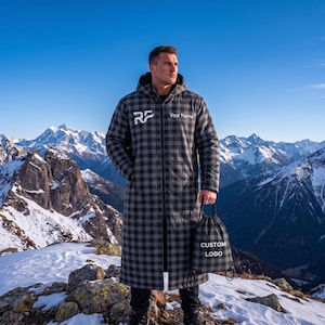 May include: A long, hooded, grey and black plaid coat with a front zipper. The chest features the white text 'RF' and 'Your Name'. A matching grey and black plaid drawstring bag is held in one hand, displaying the white text 'CUSTOM LOGO'.