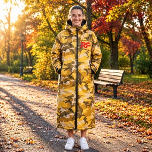 May include: A long, hooded, insulated coat featuring a yellow, brown, and tan camouflage pattern. The coat has a full-length black front zipper and the red letters RF printed on the upper left chest. It is worn with white sneakers.