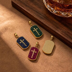 Puede incluir: Cuatro colgantes rectangulares de oro con esquinas redondeadas. Tres colgantes presentan un crucifijo de oro central sobre una cuadrícula de pequeñas piedras cuadradas en verde oscuro, azul real y rojo oscuro. Un colgante tiene un reverso de oro texturizado.