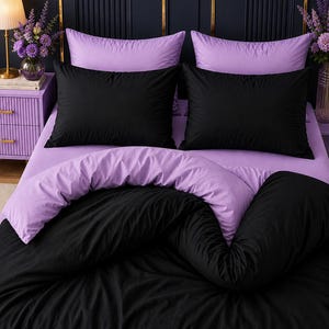 Può includere: Un set di biancheria da letto composto da un copripiumino nero a tinta unita e federe nere abbinate, sovrapposte a un lenzuolo con angoli e federe color viola chiaro. La biancheria presenta una texture del tessuto liscia e opaca.