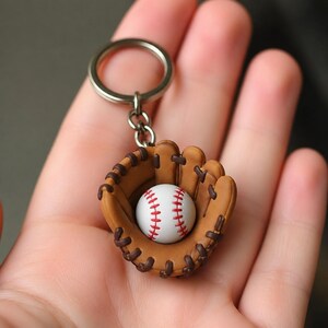 Peut inclure: Un porte-clés représentant un gant de baseball miniature marron avec des lacets marron foncé et une petite balle de baseball blanche avec des coutures rouges nichée dans la poche. L'accessoire est fixé à un anneau en métal argenté.