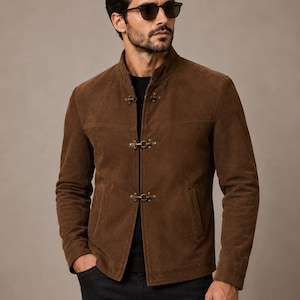 May include: A brown suede jacket featuring a stand-up collar and three antique brass toggle closures down the front. The jacket has long sleeves, a straight hem, and two side pockets. It is worn over a black shirt and black pants.