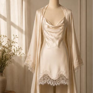May include: A champagne-colored satin slip dress and matching robe set. The slip dress features a cowl neckline and a scalloped lace hem. The long-sleeved robe includes matching lace trim on the cuffs, creating a coordinated sleepwear ensemble.