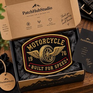 May include: A rectangular embroidered patch with rounded corners featuring a black background, gold border, and gold text reading MOTORCYCLE, 19, 76, and BUILT FOR SPEED. The center displays a gold winged tire graphic inside a cardboard shipping box.
