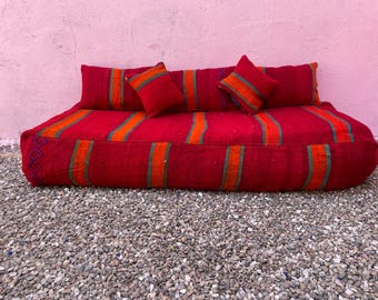 May include: A large rectangular floor cushion in deep red featuring vertical orange and green stripes. The cushion is accompanied by two matching rectangular bolster pillows and two smaller square pillows, all sharing the same red, orange, and green striped pattern.