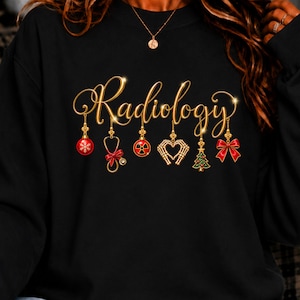 Op de afbeelding: Een zwart sweatshirt met de gouden tekst Radiology. Aan de letters hangen kerstversieringen, waaronder een rode kerstbal met sneeuwvlokken, een stethoscoop met een rode strik, een stralingssymbool, een hart van skelettenhanden, een kerstboom en een rode strik.