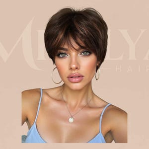 May include: A short, layered dark brown wig with subtle highlights and wispy bangs. The hair is styled in a textured, voluminous pixie cut. The background features the text MILYA HAIR in a light, elegant font against a soft beige backdrop.