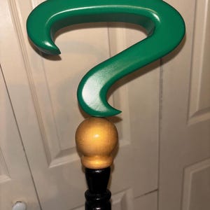 May include: A green question mark shaped cane with a gold ball on top and a black wooden shaft.