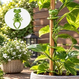 Puede incluir: Un clip para plantas en forma de rana de color verde mate diseñado para envolverse alrededor de un tutor de madera. El accesorio presenta una rana estilizada con extremidades extendidas que se sujetan para sostener tallos de plantas.