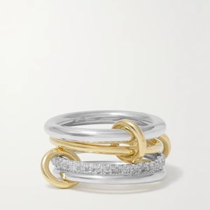 Op de afbeelding: Een ring met meerdere banden bestaande uit een combinatie van gepolijste zilverkleurige en goudkleurige metalen ringen die met elkaar verbonden zijn. Eén van de zilverkleurige banden is bezet met kleine, heldere, fonkelende steentjes.