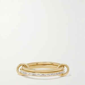 May include: An 18K yellow gold ring featuring two interlocking bands. One band is a plain polished gold hoop, while the other is set with a row of clear baguette-cut stones. The interior of the plain band is engraved with the letters SK and 18K.
