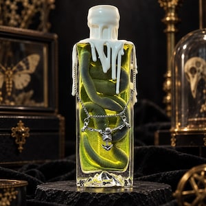 Peut inclure: Une bouteille en verre rectangulaire remplie d'un liquide jaune vif avec un serpent vert enroulé à l'intérieur. Le haut de la bouteille est recouvert de gouttes de cire blanche. Un collier à chaîne argentée avec un pendentif squelette.