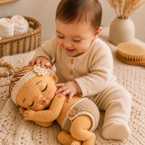 May include: A handmade crochet doll featuring a sleeping expression, light tan yarn skin, a white headband with a flower accent, and a beige nappy with a small wooden button. The doll is crafted with detailed stitching and has a soft, textured appearance.