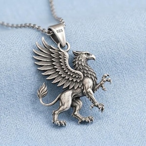 Peut inclure: Un collier pendentif argenté représentant un griffon détaillé avec des ailes déployées, un corps de lion et une tête d'aigle. La bélière en métal porte l'inscription 925, indiquant de l'argent sterling, et le pendentif est suspendu à une chaîne.