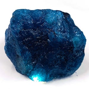 Peut inclure: Un spécimen minéral brut et non poli présentant une couleur bleu profond et saturé. La pierre possède une surface irrégulière et dentelée avec des sections translucides qui captent la lumière, révélant des nuances de bleu foncé et vif.