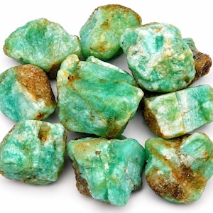Pode incluir: Uma coleção de pedras de esmeralda brutas e não polidas com uma cor verde vibrante e inclusões minerais naturais castanhas e brancas. Estes cristais rugosos e irregulares variam em forma e tamanho, exibindo uma textura cristalina e superfícies opacas a translúcidas.