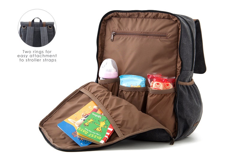 May include: A gray canvas diaper bag backpack with multiple pockets and a brown interior. The backpack is open and shows a baby bottle, wipes, and snacks inside. The backpack has two rings on the top for attaching to a stroller.