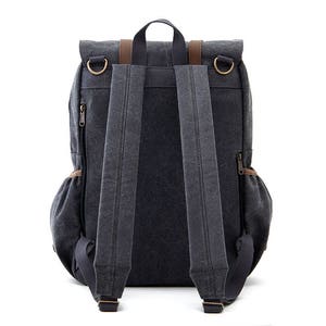 May include: A dark gray canvas backpack with brown leather accents and adjustable straps. The backpack has a flap closure with two buckles and a zippered pocket on the front.