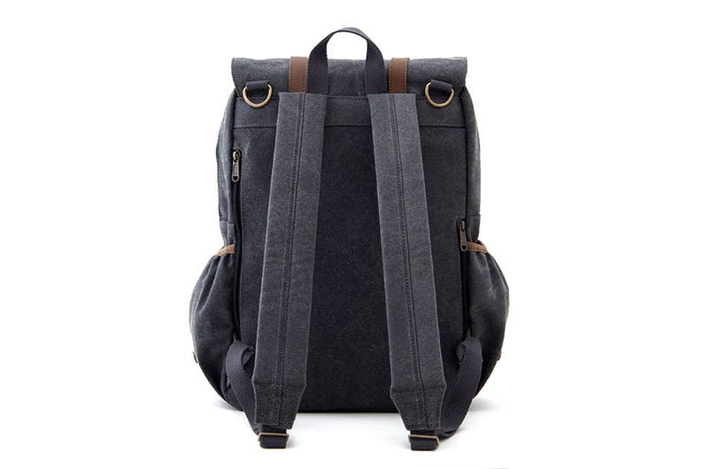 May include: A dark gray canvas backpack with brown leather accents and adjustable straps. The backpack has a flap closure with two buckles and a zippered pocket on the front.