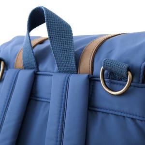 May include: A blue backpack with brown leather accents and gold metal hardware. The backpack has two adjustable straps and a top handle.