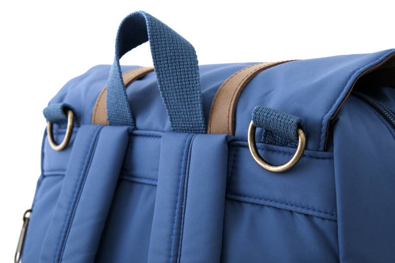 May include: A blue backpack with brown leather accents and gold metal hardware. The backpack has two adjustable straps and a top handle.