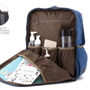 May include: A blue backpack with multiple pockets and compartments. The backpack has a brown interior and features two rings for easy attachment to stroller straps. The backpack is open and shows a magazine, a water bottle, and two bottles of lotion inside.