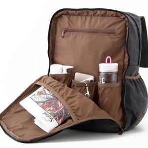 May include: A black canvas backpack with multiple pockets and compartments. The backpack is open and shows a magazine, a water bottle, and other items inside.