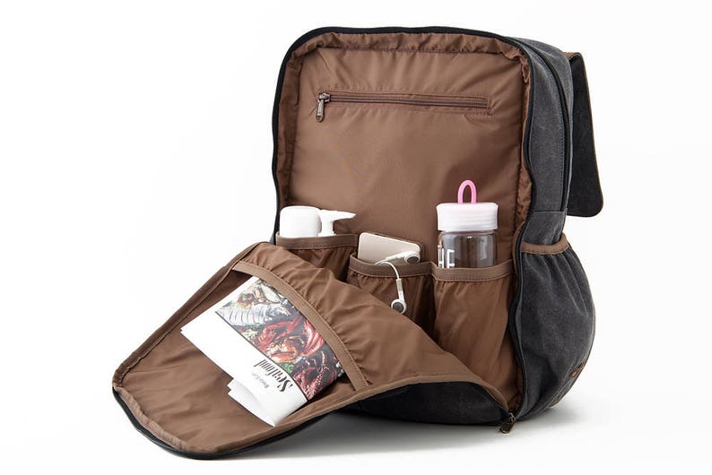 May include: A black canvas backpack with multiple pockets and compartments. The backpack is open and shows a magazine, a water bottle, and other items inside.