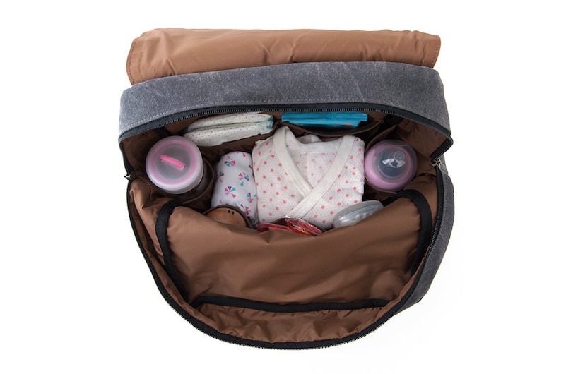 May include: A gray canvas diaper bag with brown accents is open and filled with baby items, including a white onesie with pink polka dots, a blue and white patterned cloth, and two pink bottles.