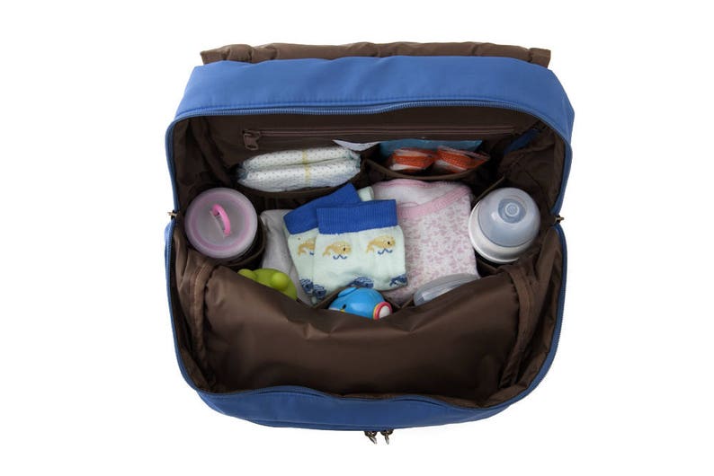 May include: A blue diaper bag with a brown interior. The bag is open and filled with baby items, including diapers, socks, a bottle, and a toy.