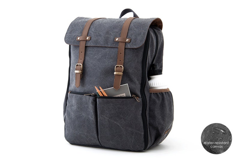 May include: A gray canvas backpack with brown leather straps and buckles. The backpack has a large main compartment and a smaller front pocket. The backpack is water-resistant.
