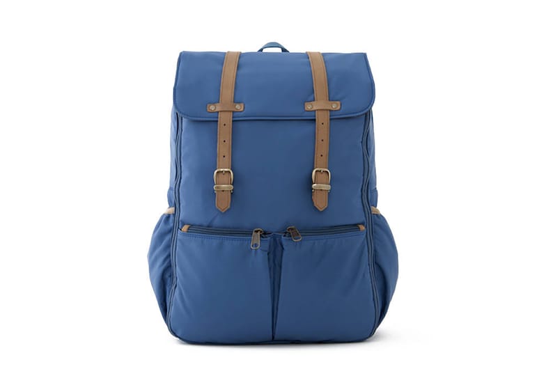 May include: A blue canvas backpack with brown leather straps and buckles. The backpack has two large front pockets with zippers.