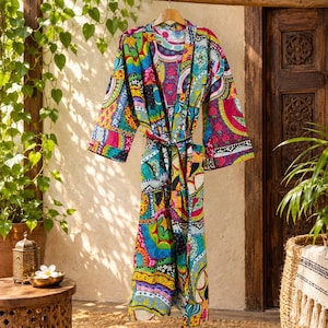 May include: A long-sleeved robe featuring a vibrant, multi-colored patchwork pattern with intricate floral and geometric motifs in shades of magenta, turquoise, yellow, and black. The garment includes a matching tie belt and wide sleeves.