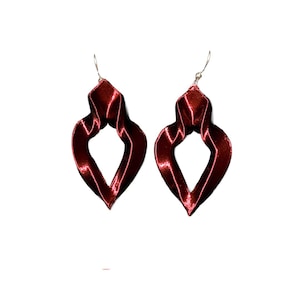 Può includere: Un paio di orecchini rosso scuro con finitura satinata e un design attorcigliato a forma di goccia. Ogni orecchino è appeso a un sottile gancio in metallo argentato, mostrando una superficie liscia e riflettente con contorni scultorei.