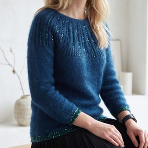 May include: A deep blue long-sleeved sweater featuring a round neckline and a fuzzy, textured knit. The garment is embellished with vertical rows of shimmering green sequins around the yoke, as well as horizontal bands of green sequins at the cuffs.