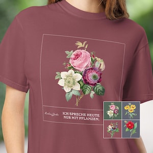 Könnte beinhalten: Ein kastanienbraunes T-Shirt mit einer quadratischen Grafik, die eine botanische Illustration von rosa, weißen und violetten Blumen zeigt. Unter den Blumen steht der Text: "Loudian Garden" und "ICH SPRECHE HEUTE NUR MIT PFLANZEN." Ein kleiner Einschub zeigt vier Blumenmotive.