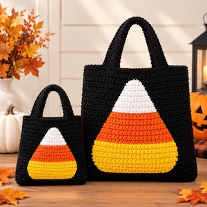 May include: Two black crochet tote bags of different sizes, each featuring a large, centered candy corn graphic. The candy corn design consists of a white top section, an orange middle section, and a yellow bottom section, all textured.