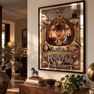 Könnte beinhalten: Ein gerahmtes Filmplakat für Raiders of the Lost Ark mit einer zentralen Illustration von Indiana Jones mit Fedora, umgeben von kleineren Charakterporträts, einer Landkarte, Totenköpfen und dem Filmtitel in großen, stilisierten weißen Buchstaben.