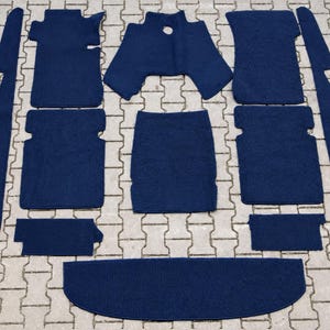 Peut inclure: Un ensemble complet de tapis de sol et de pièces de garniture intérieure pour automobile en moquette bleu foncé. La collection comprend diverses formes rectangulaires et profilées conçues pour couvrir le sol et les panneaux latéraux.