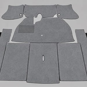 Puede incluir: Un juego de alfombrillas grises para automóvil con acabado de moqueta texturizada. La colección incluye varias piezas con bordes ribeteados, una almohadilla rectangular para el talón en la alfombrilla del conductor y recortes circulares.