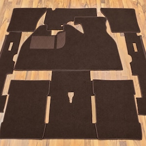 Peut inclure: Un ensemble de tapis de sol automobiles marron foncé avec une surface en velours texturé et des bordures assorties. Le lot comprend plusieurs pièces découpées pour couvrir l'intérieur du véhicule, dont une grande section centrale.