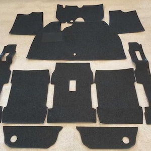 May include: A complete set of black automotive floor mats featuring a textured, carpeted surface. The collection includes various shaped pieces designed for vehicle interior coverage, including front and rear sections with specific cutouts.