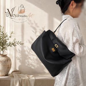 Puede incluir: Un bolso de hombro de cuero negro con una solapa rectangular, un cierre de giro de metal dorado y una sola correa para el hombro. El bolso tiene un acabado liso y mate y una silueta estructurada sobre un fondo neutro.
