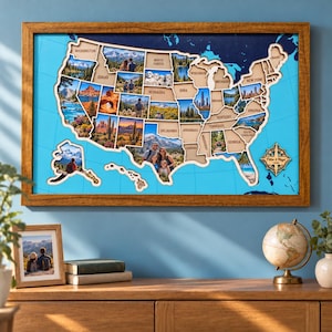 May include: A wooden framed wall map of the United States featuring a light blue background with dark blue ocean details. The map includes cutouts for each state, many of which contain photographic inserts of landscapes and people.