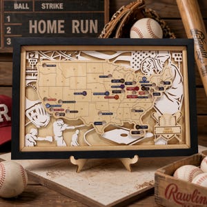 Könnte beinhalten: Eine gerahmte, mehrschichtige Holzkarte der Vereinigten Staaten mit Baseballstadion-Standorten, eingravierten Länderkürzeln sowie ausgeschnittenen Illustrationen von Spielern, Handschuhen und einem Baseball. Eine Plakette zeigt Terry's Stadium Map.
