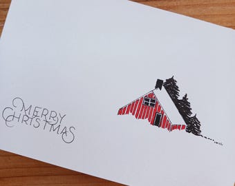 May include: A white greeting card featuring a black ink illustration of a red cabin with a snow-covered roof, surrounded by black pine trees. The text Merry Christmas is written in black cursive lettering on the left side of the card.