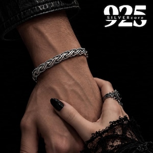 Könnte beinhalten: Ein Armband aus Sterlingsilber mit gedrehtem Seildesign und oxidierten Details. Das Armband wird am Handgelenk getragen, dazu ein Silberring mit einem dunklen Stein. Der Text 925 SILVERcore ist in der oberen rechten Ecke zu sehen.