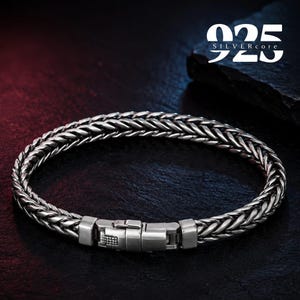 May include: A silver wheat chain bracelet featuring a polished metal box clasp closure. The bracelet has a textured, braided link design with a metallic finish. The text 925 SILVERcore is visible in the upper right corner of the image.